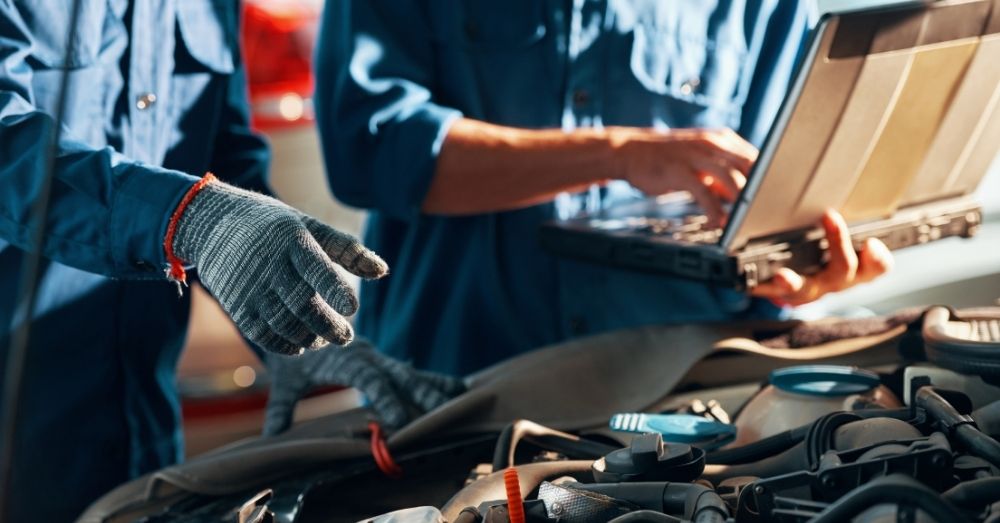 Two mechanics diagnose a car engine with a laptop.