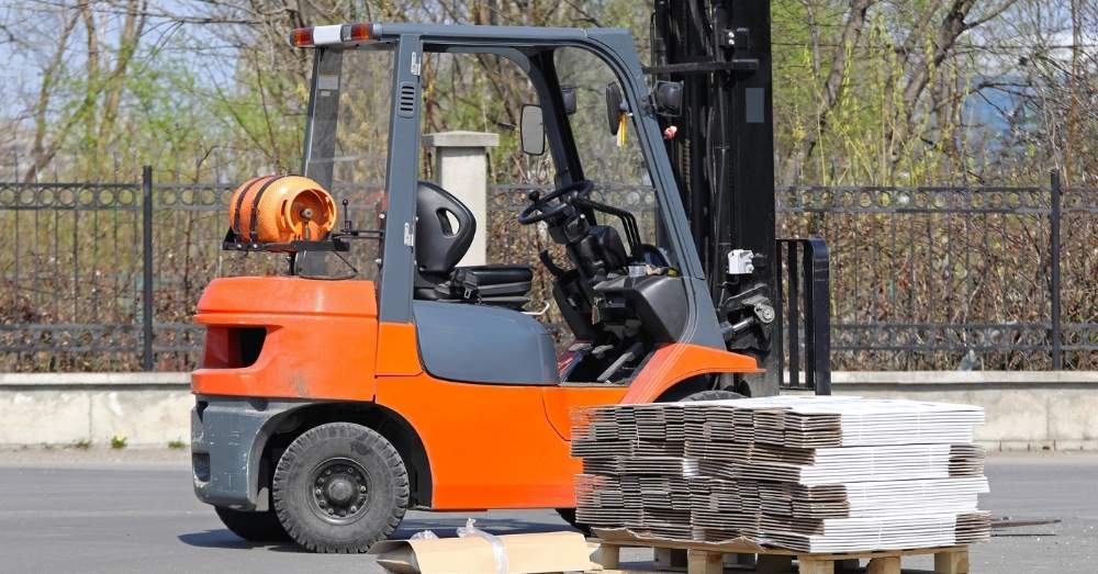 An orange forklift sits beside a stack of cardboard boxes.