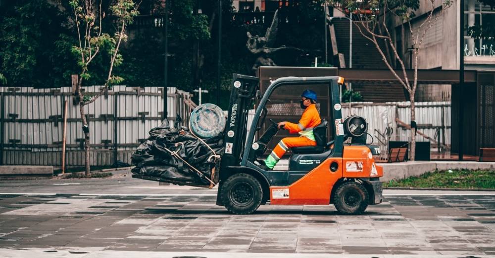 Worker driving a forklift carrying heavy materials in an outdoor construction site.