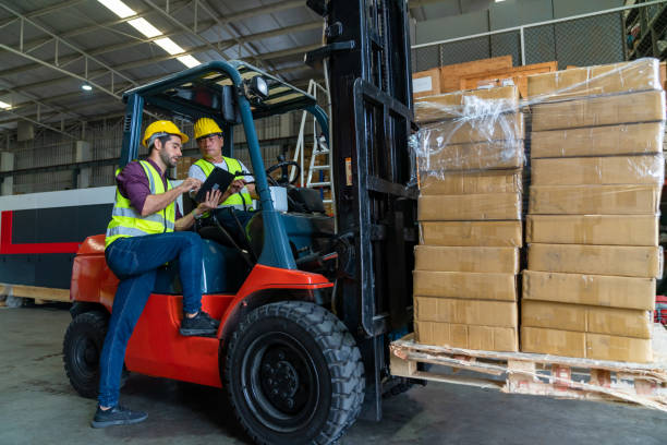 Two warehouse workers wearing safety helmets and vests reviewing a checklist