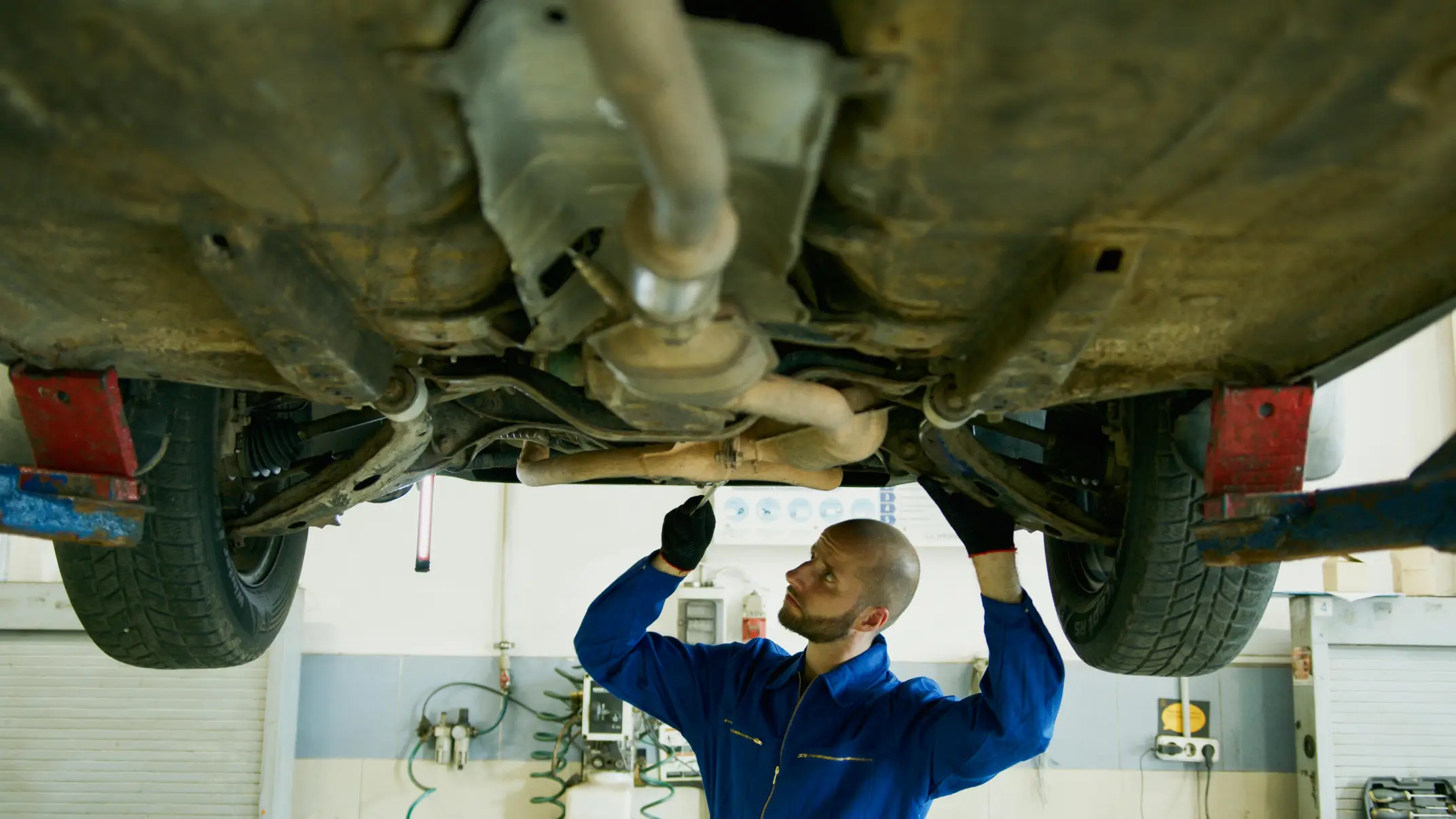 Auto mechanic inspecting and repairing a vehicle’s exhaust system from underneath a car