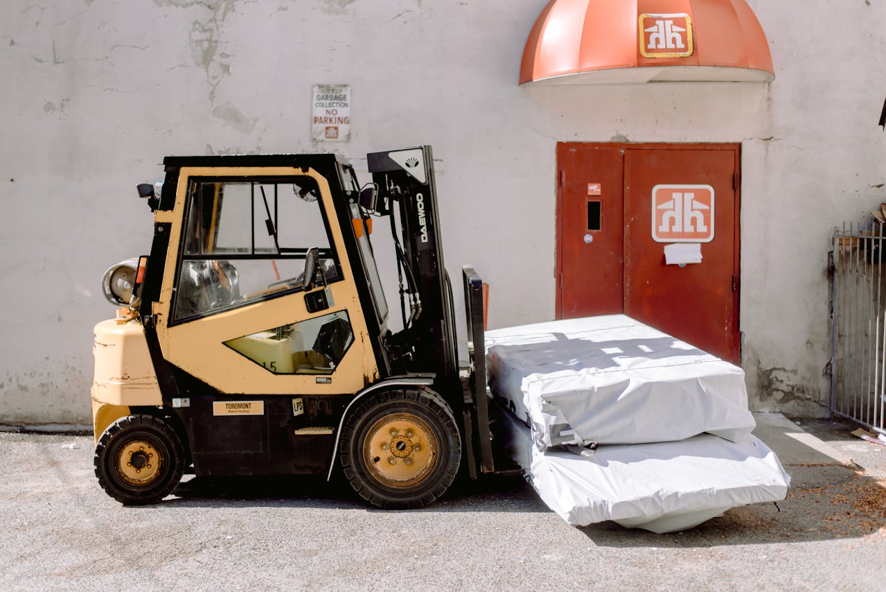 Yellow and black Daewoo forklift parked in front of a building, carrying white tarp-covered materials.