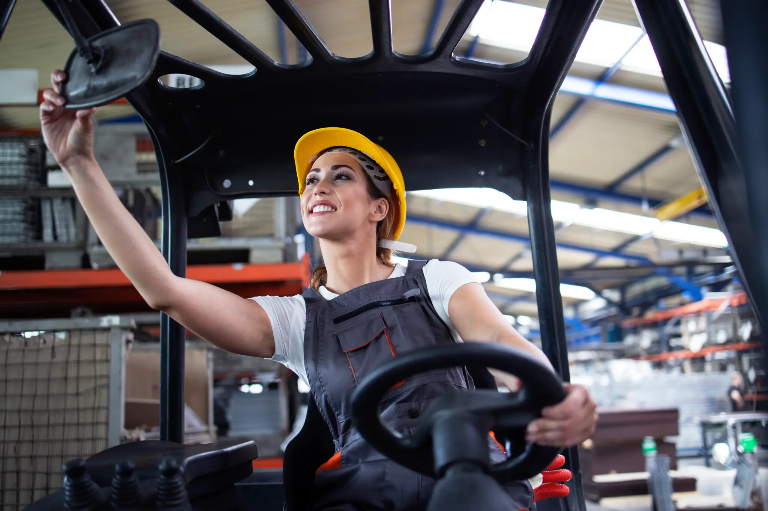 Smiling female warehouse worker adjusting the rearview mirror while sitting in a forklift